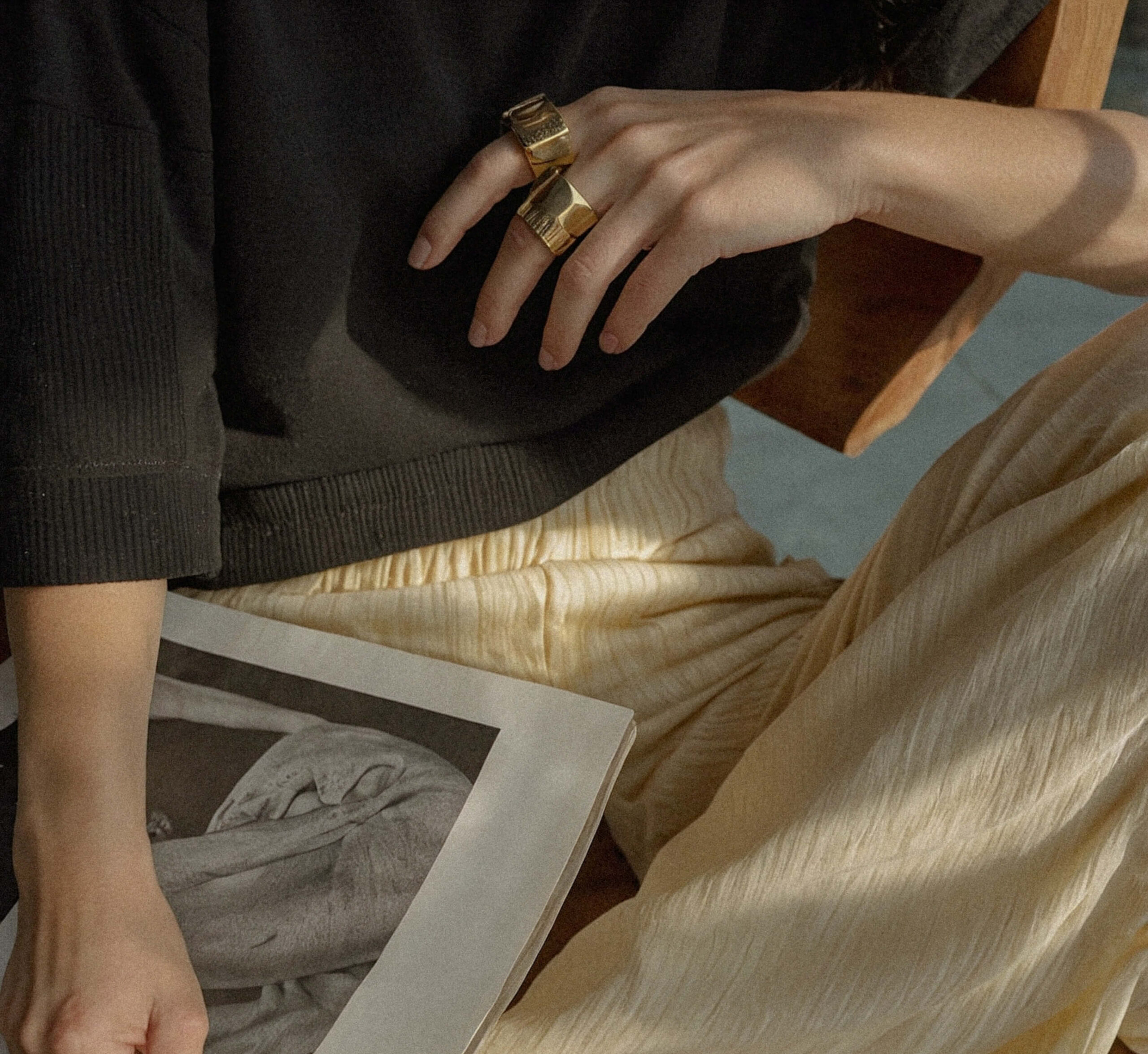 A person wearing gold rings and cream pleated pants holds an open magazine while seated, with part of their black top visible. An example of website design and mid-life brand design from Sweet Pea Ink Creative.