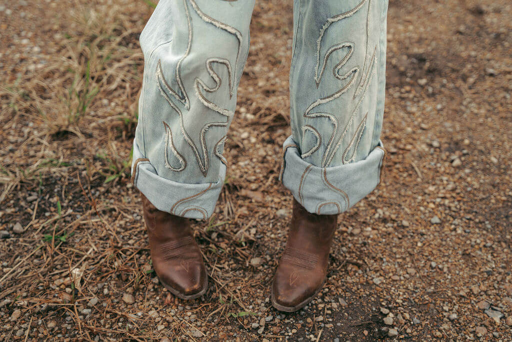 Sweet Pea Ink Creative | Brand Strategy Person wearing light-wash jeans with embroidered designs and brown leather boots standing on rocky ground—a style as distinctive as Sweet Pea Ink Creative’s brand design.