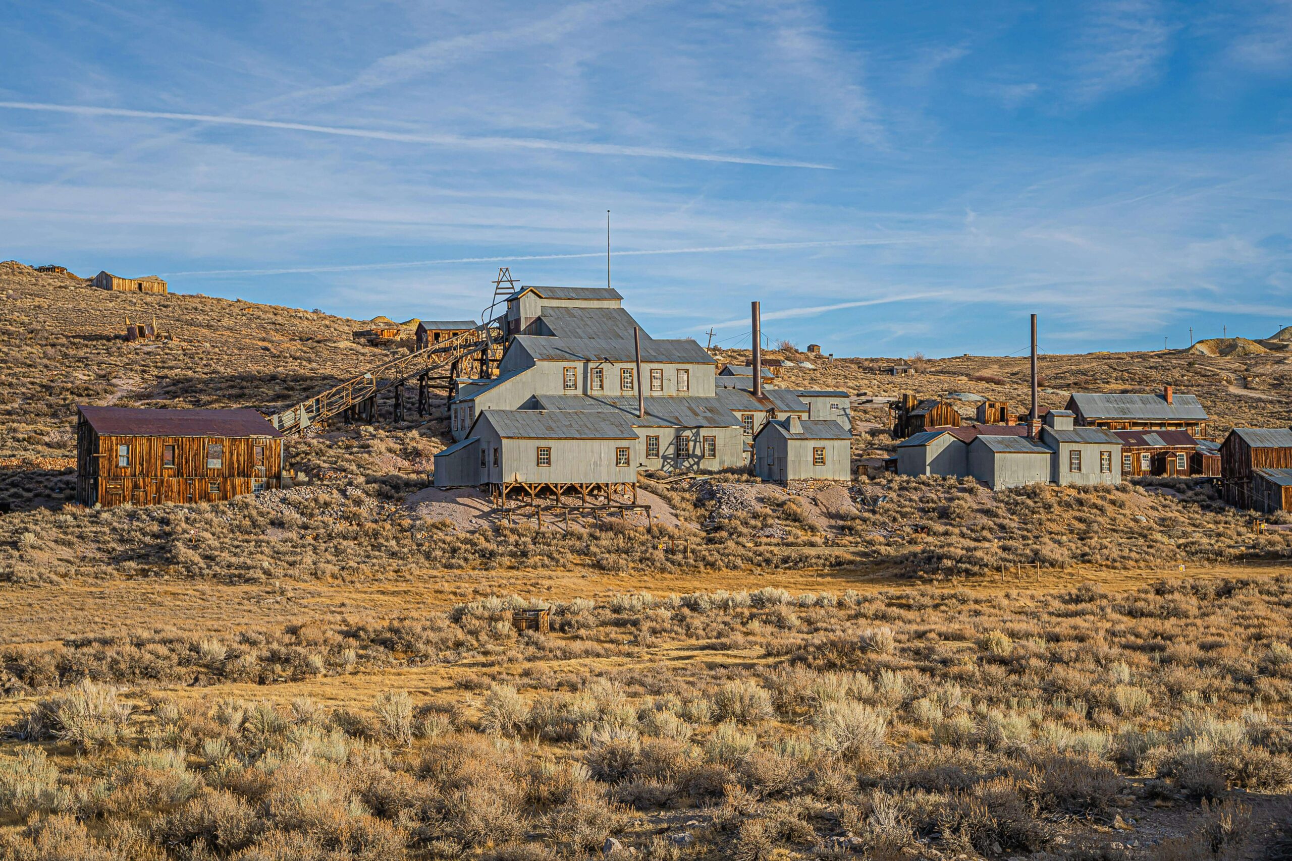 Abandoned mining buildings sit on a dry, grassy landscape under a clear blue sky in a historic ghost town—an inspiring scene for Sweet Pea Ink Creative, specialists in brand design and how to optimize your site for SEO.